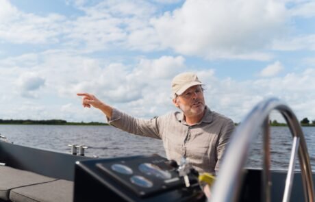 Harm aan het roer van de sloep, wijzend over het water