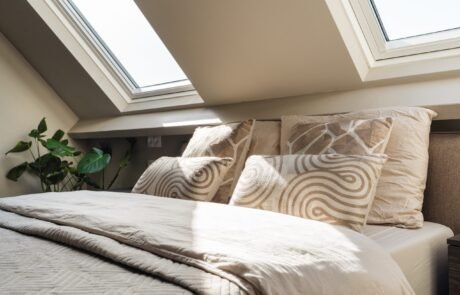 Opgemaakt bed met kussens in het ochtendlicht onder het dakraam
