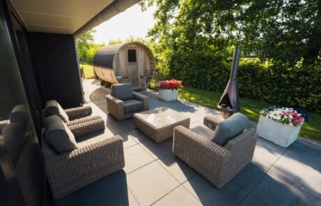 Overdekt terras met loungeset, vuurkorf en de barrelsauna in de tuin